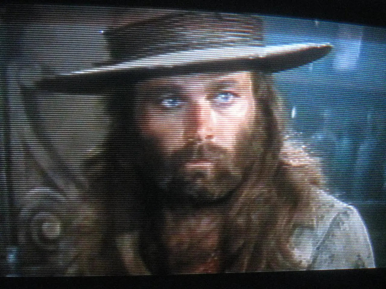 This image consists of a screen with an image of a man and he has worn a hat. He is with beard and...