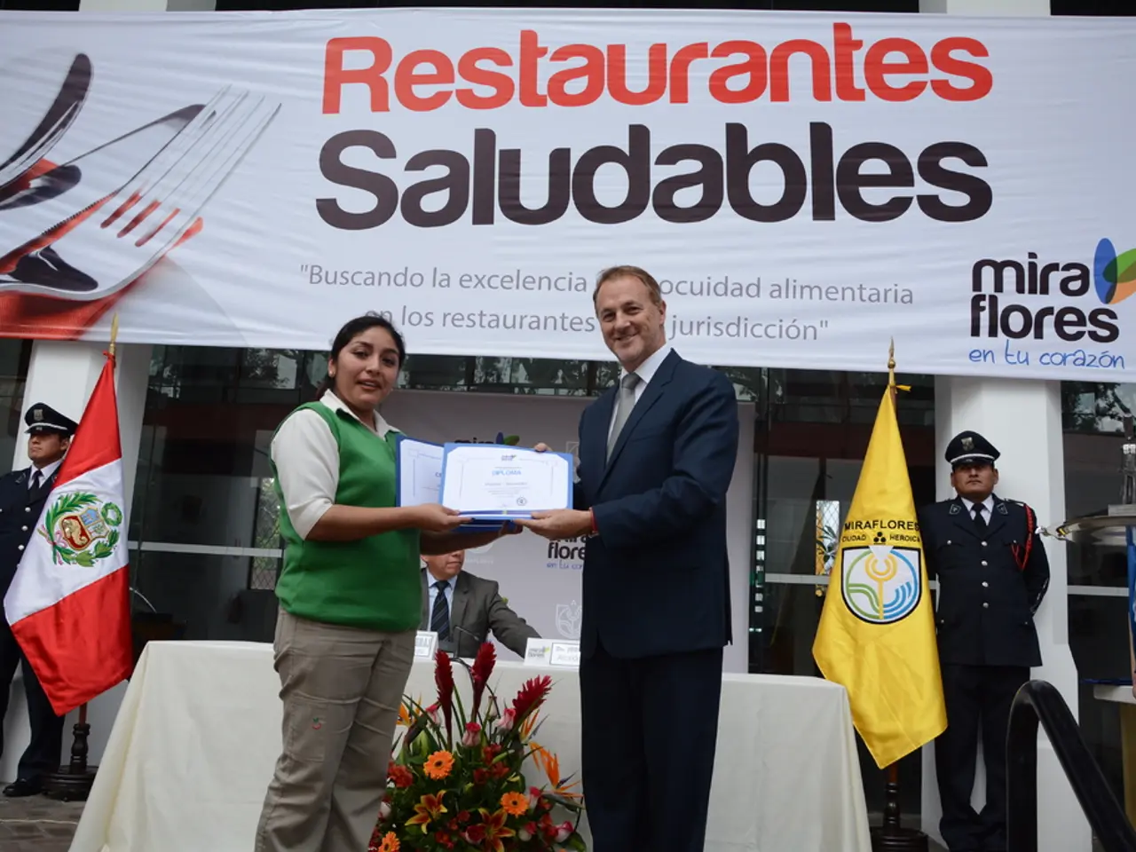 In this image, we can see a woman and man smiling and holding certificates. At the bottom of the...