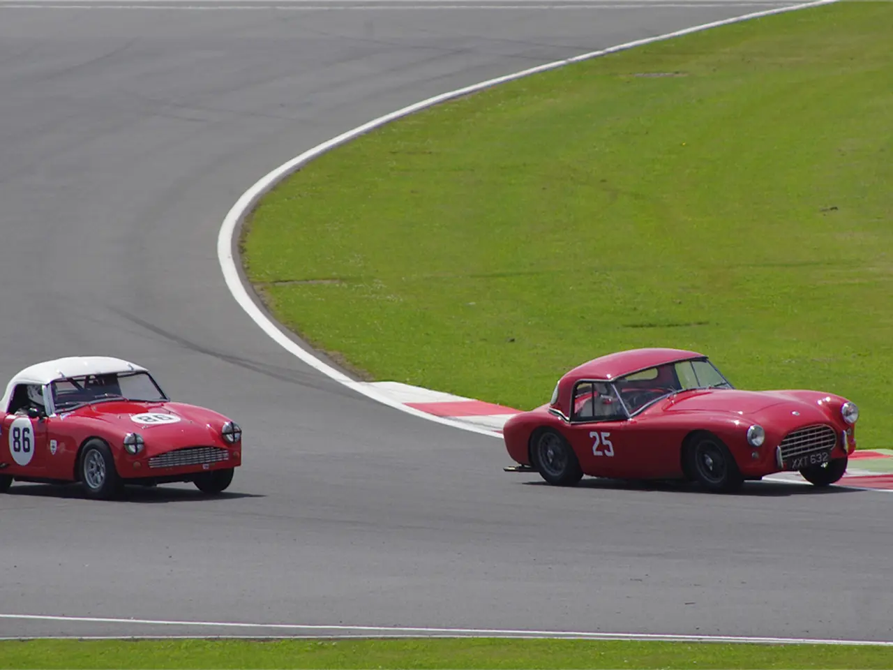 In this picture there are two red color cars, racing on the runway track. On the right side we can...