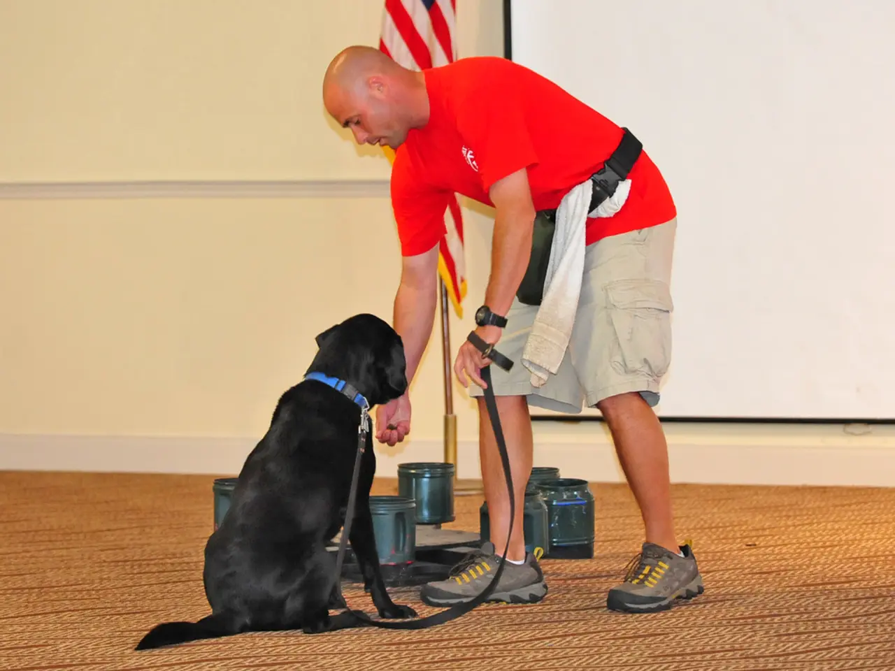 This picture describes about a man holding a dog and we can see some jars, a flag and a projector...