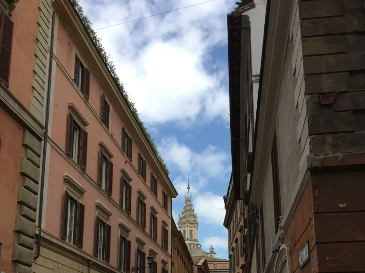 In this image there are buildings, plants and there are vehicles on the road and the sky is cloudy.