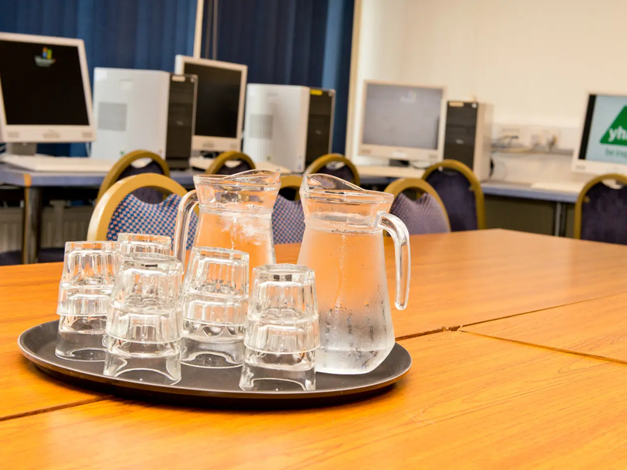 This image is clicked inside a room. There are tables, on the tables there are computers and there...