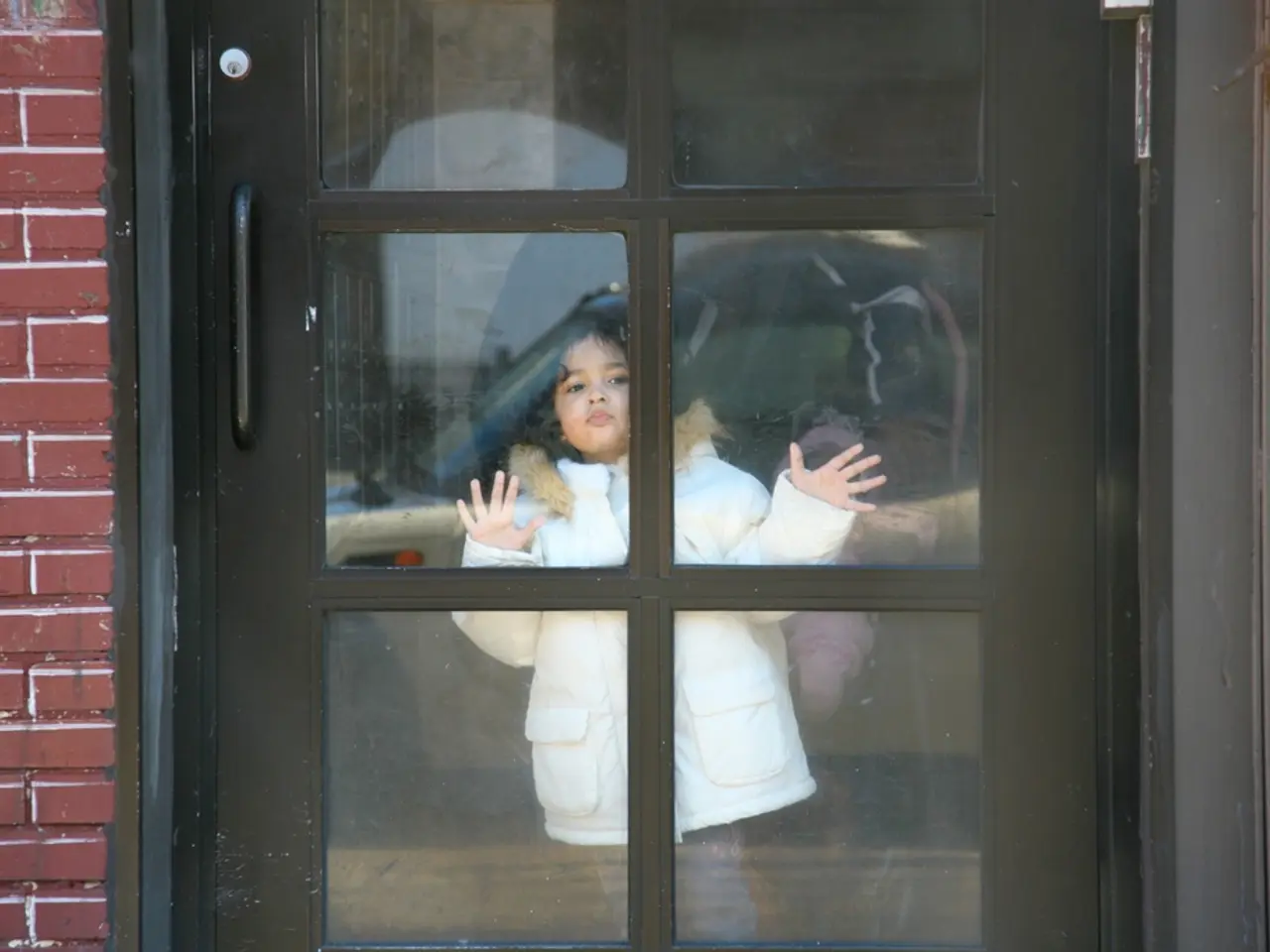 In this image there is a girl child watching outside of the glass door, beside the door there is a...