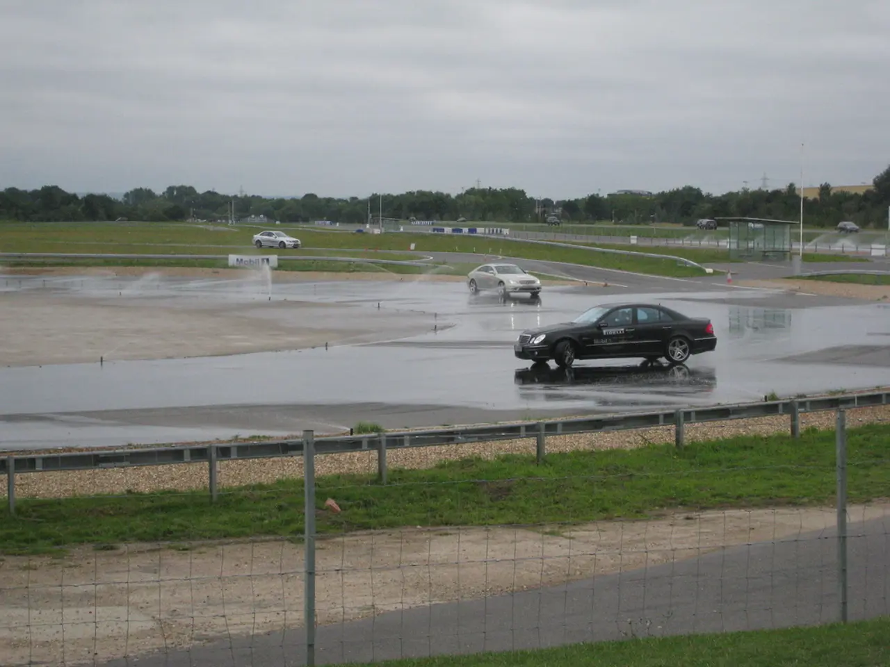 In this image, there is a fencing, there's grass on the ground at some area, there are some cars on...