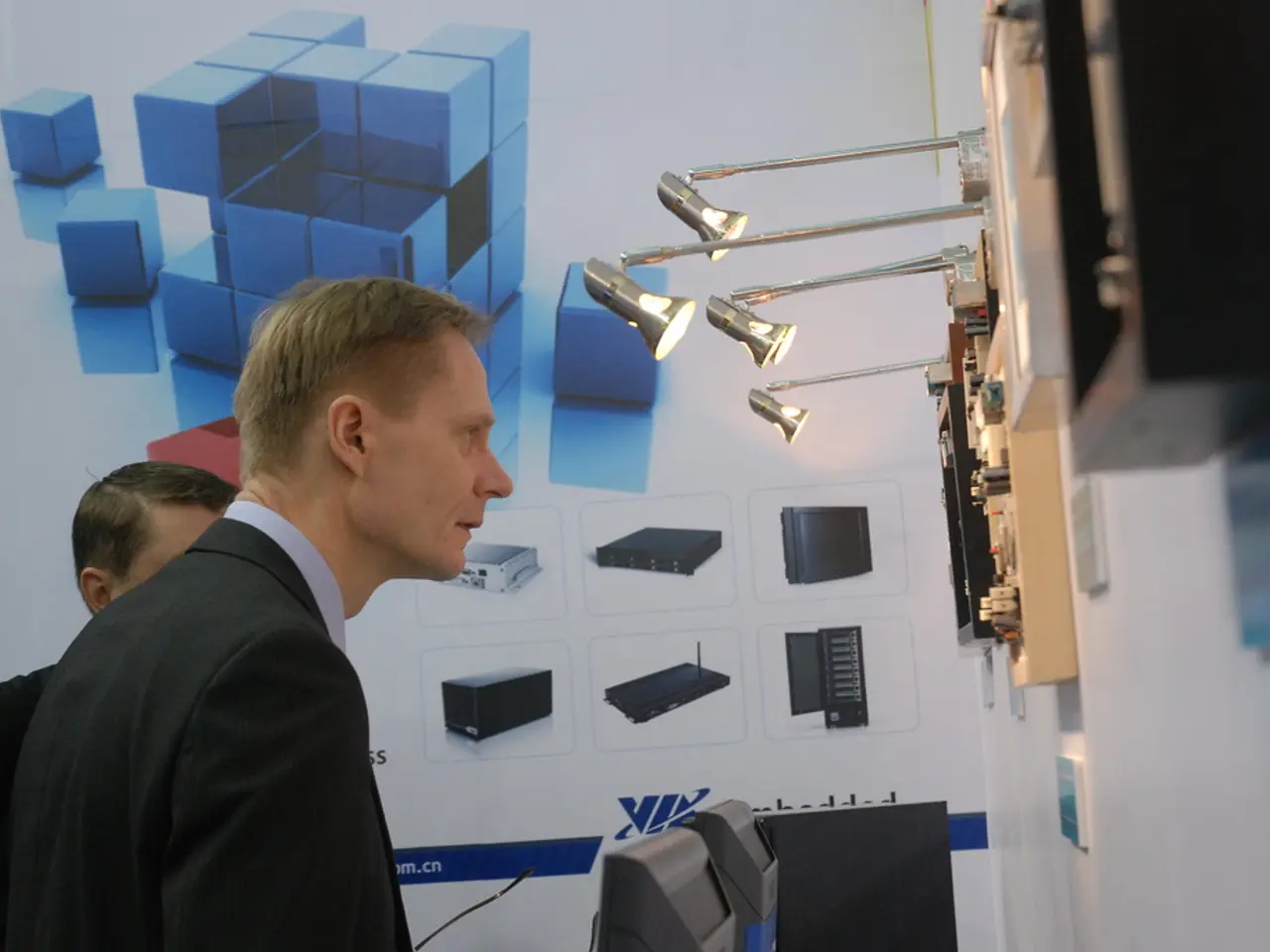 The man on the left corner of the picture wearing blue shirt and black blazer is standing and...