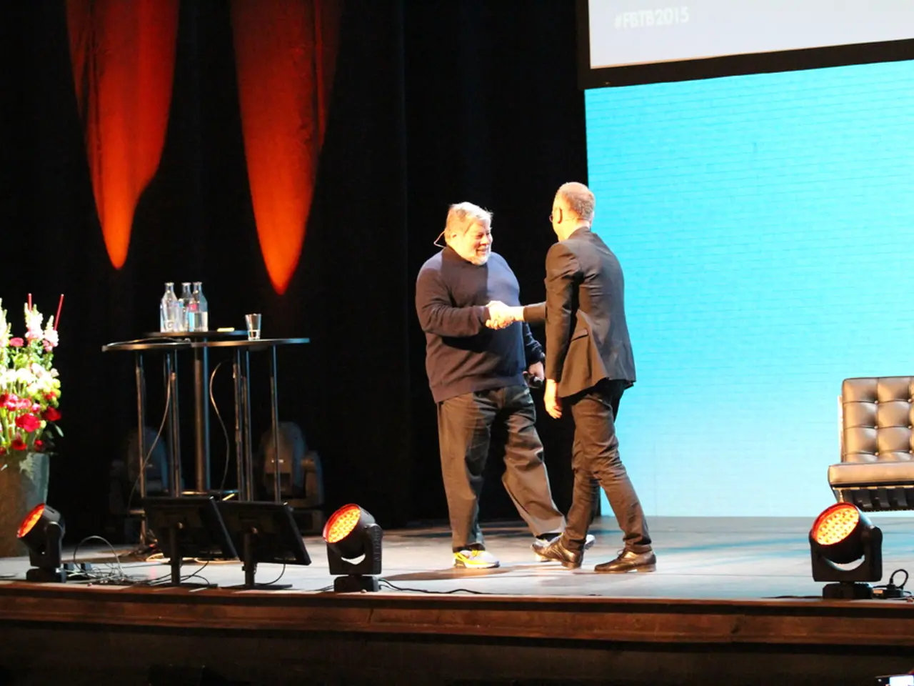 In this image in the center there is a stage, on the stage there are two persons who are standing...