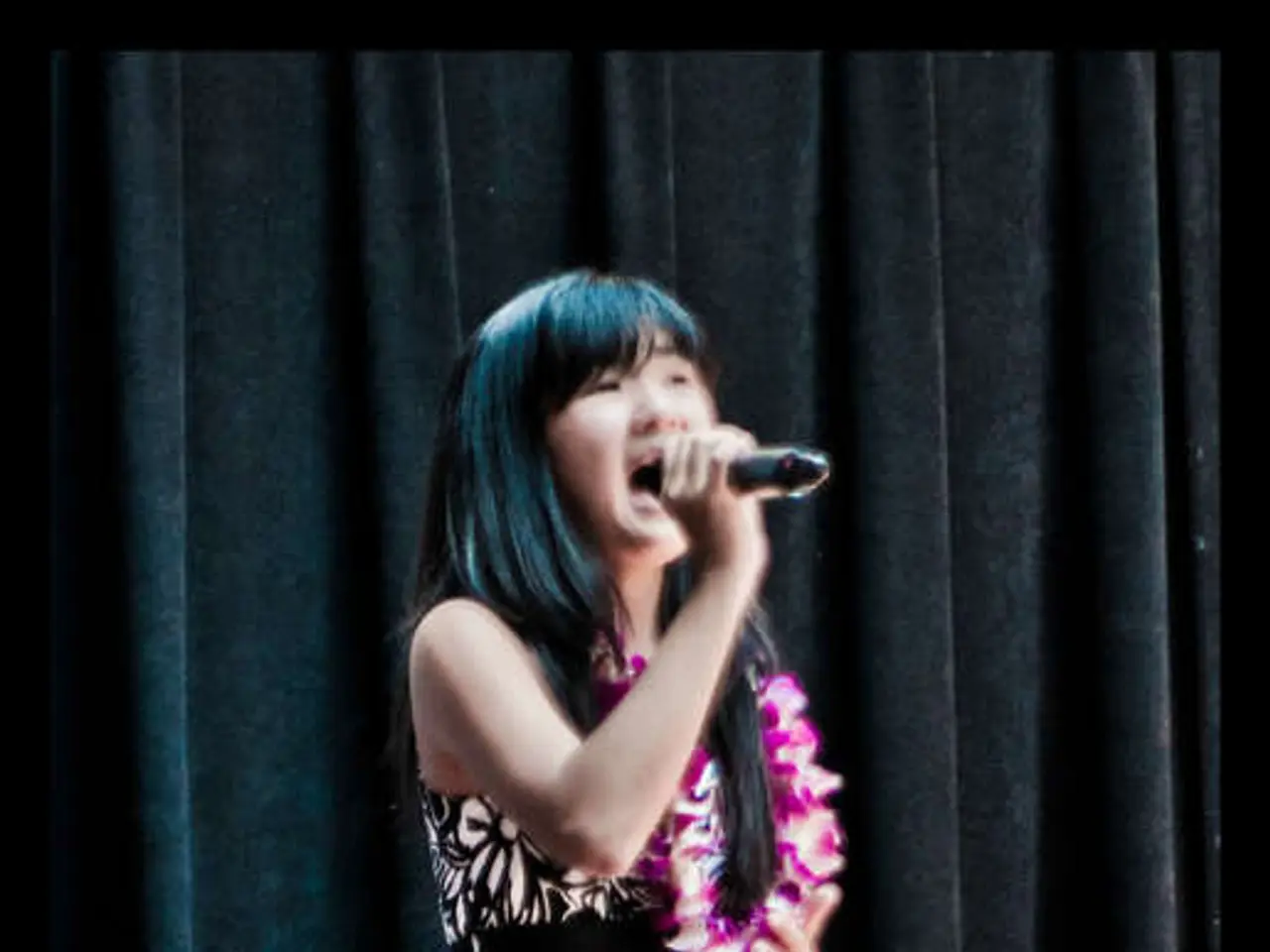 She is standing on a stage. She is holding a mic. She is singing a song. She is wearing a colorful...