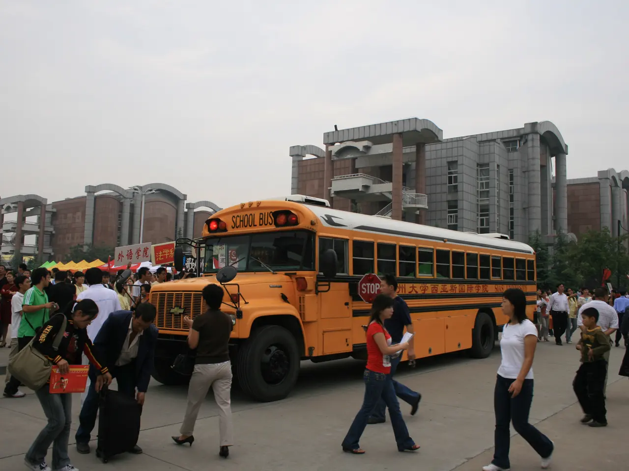 The image shows a group of people walking in front of a school bus on a road surrounded by...