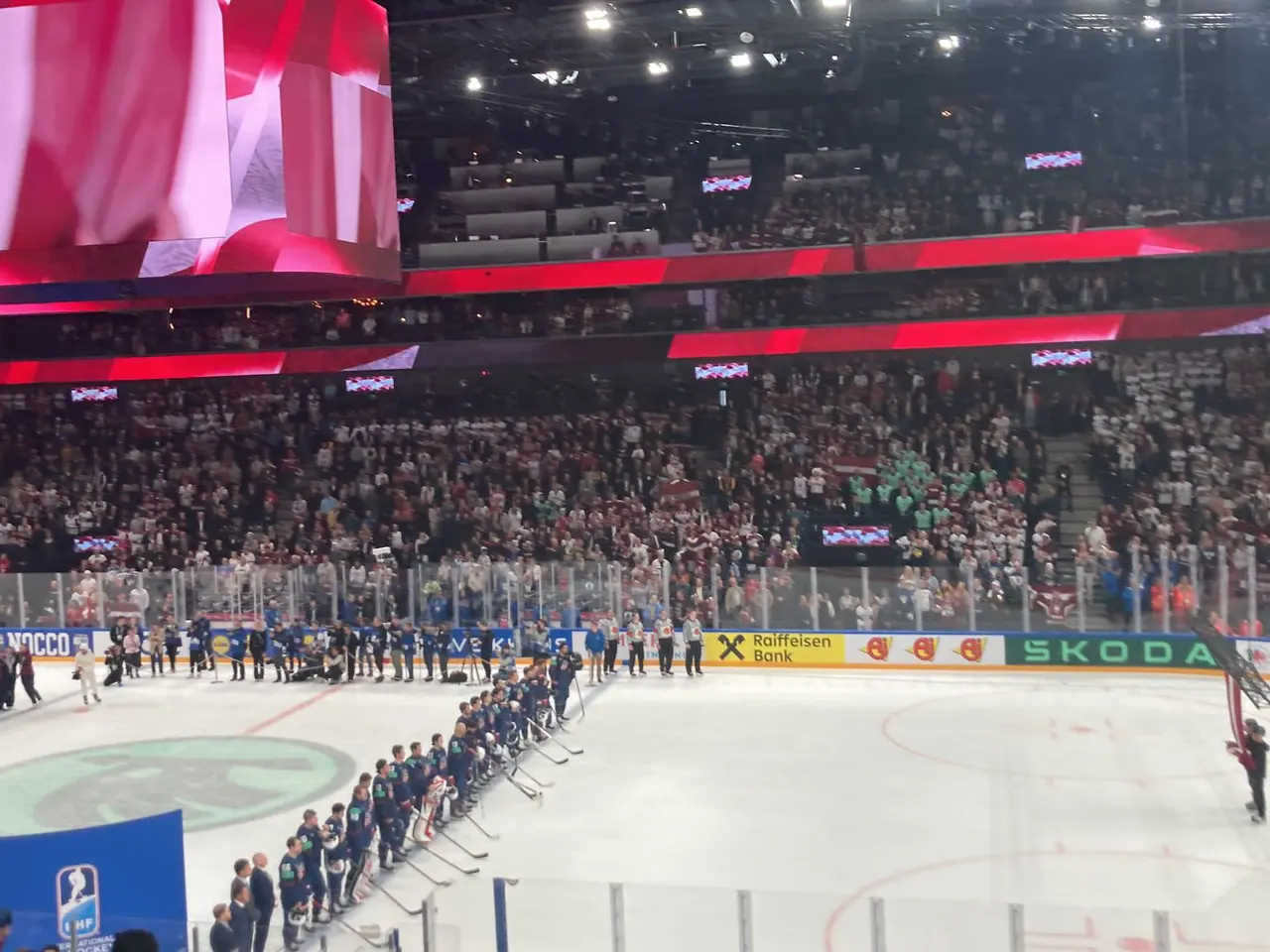 The image shows a hockey game being played in a large arena, with a group of people standing on the...