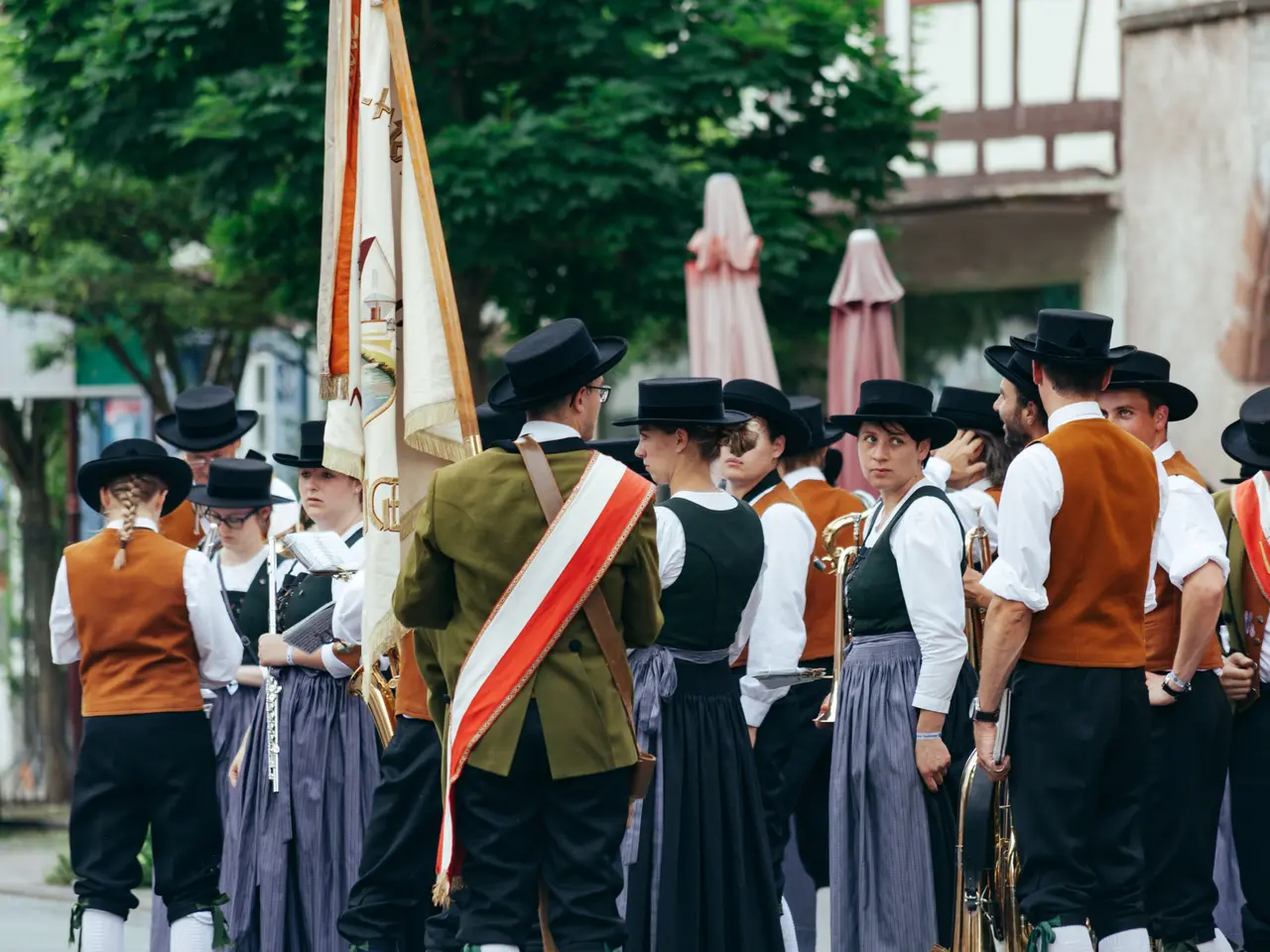 The image shows a group of people in traditional Bavarian clothing marching down a street, with...