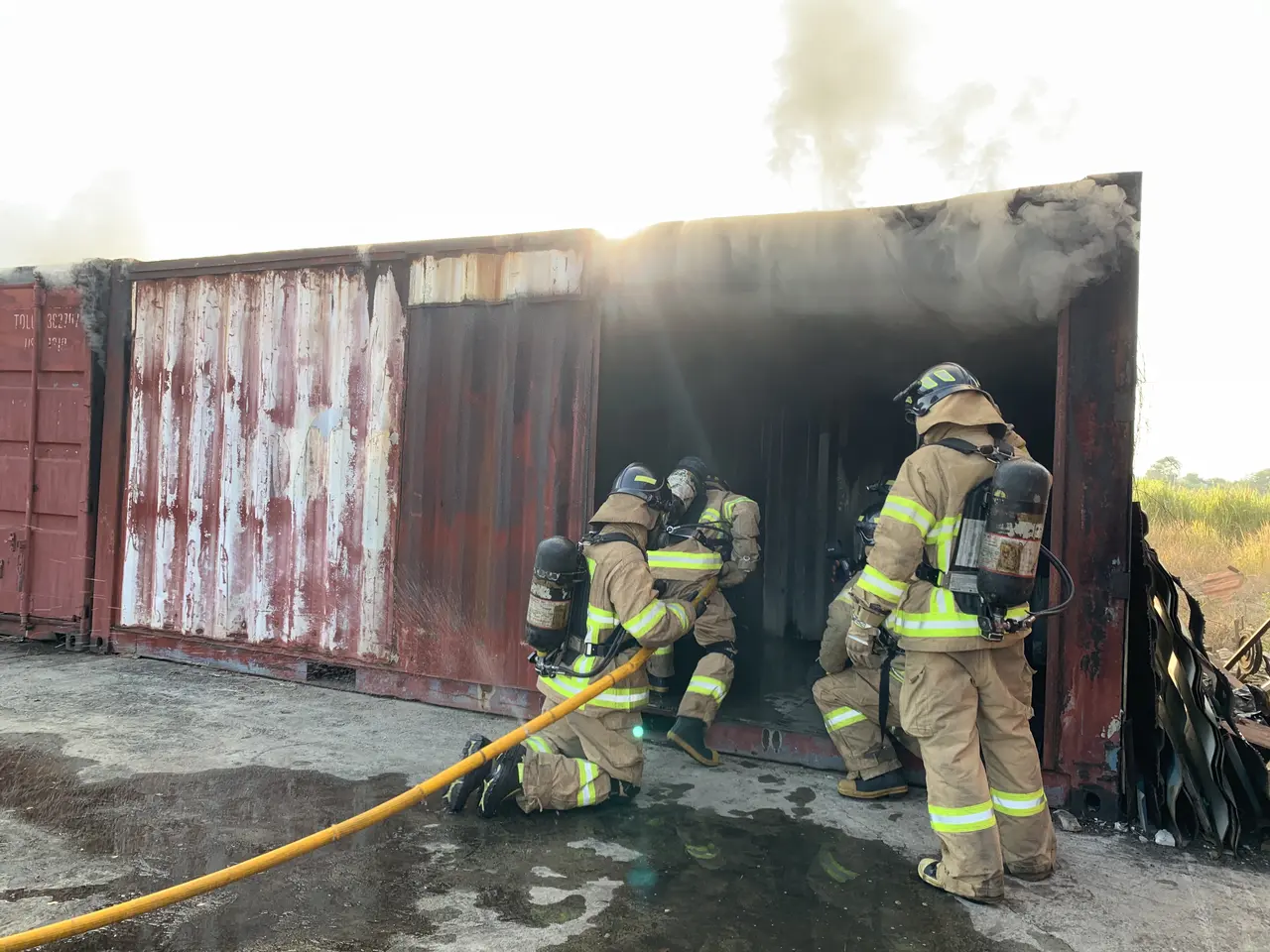 The image shows a group of firefighters wearing helmets and cylinders, working to put out a fire in...