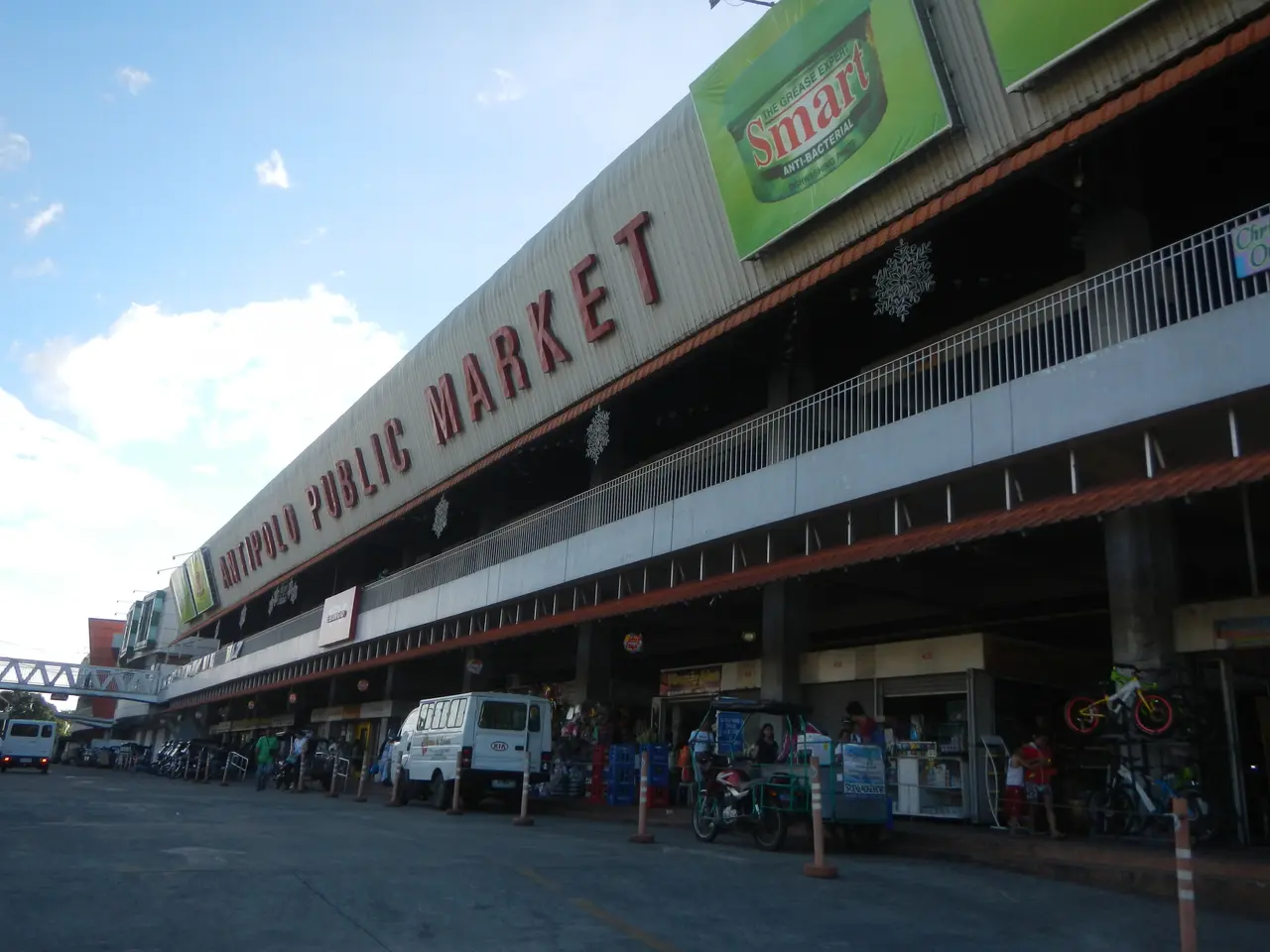 The image shows a bustling public market in the middle of a city street, with vehicles driving by,...
