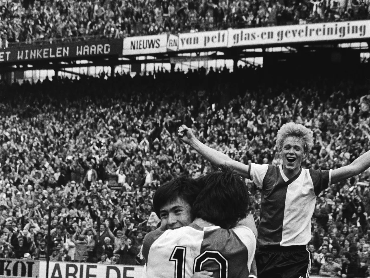 The image shows a group of three soccer players celebrating a goal in front of a large crowd in a...