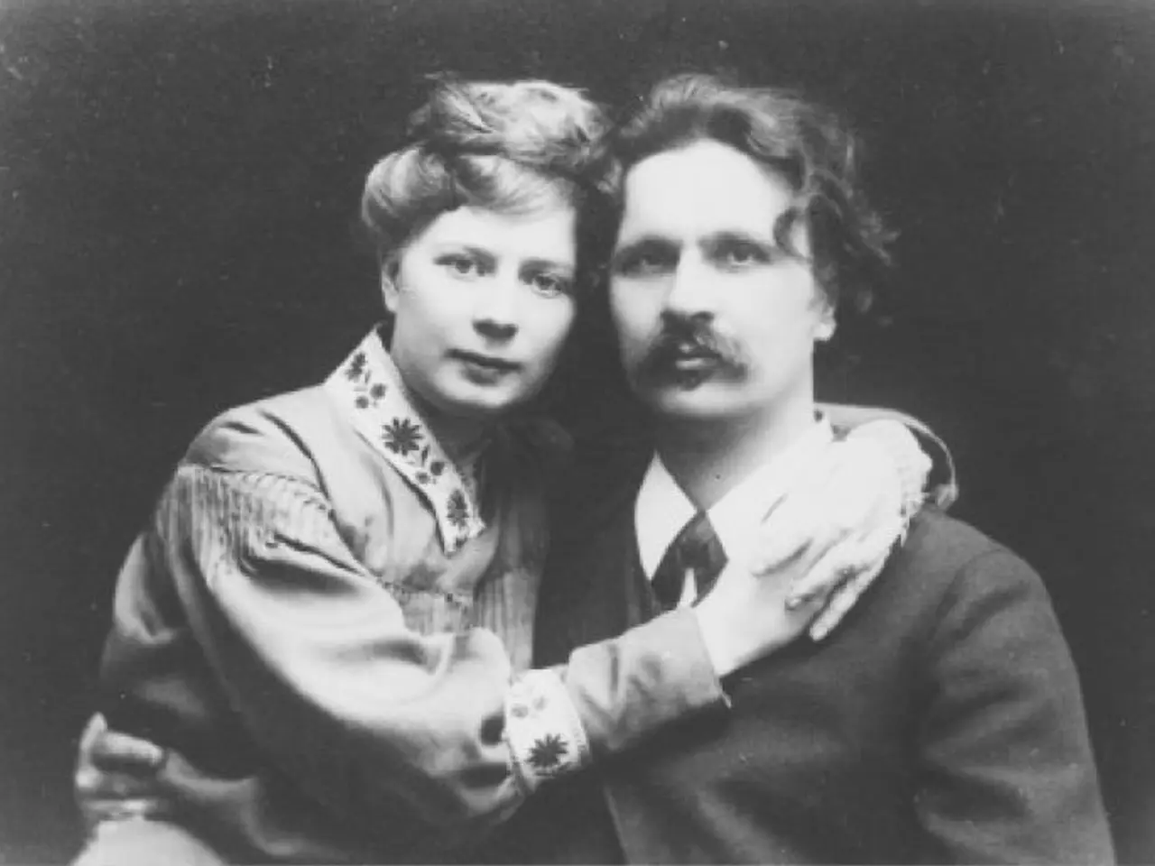 The image shows a black and white photo of a man and woman embracing each other. The man is wearing...