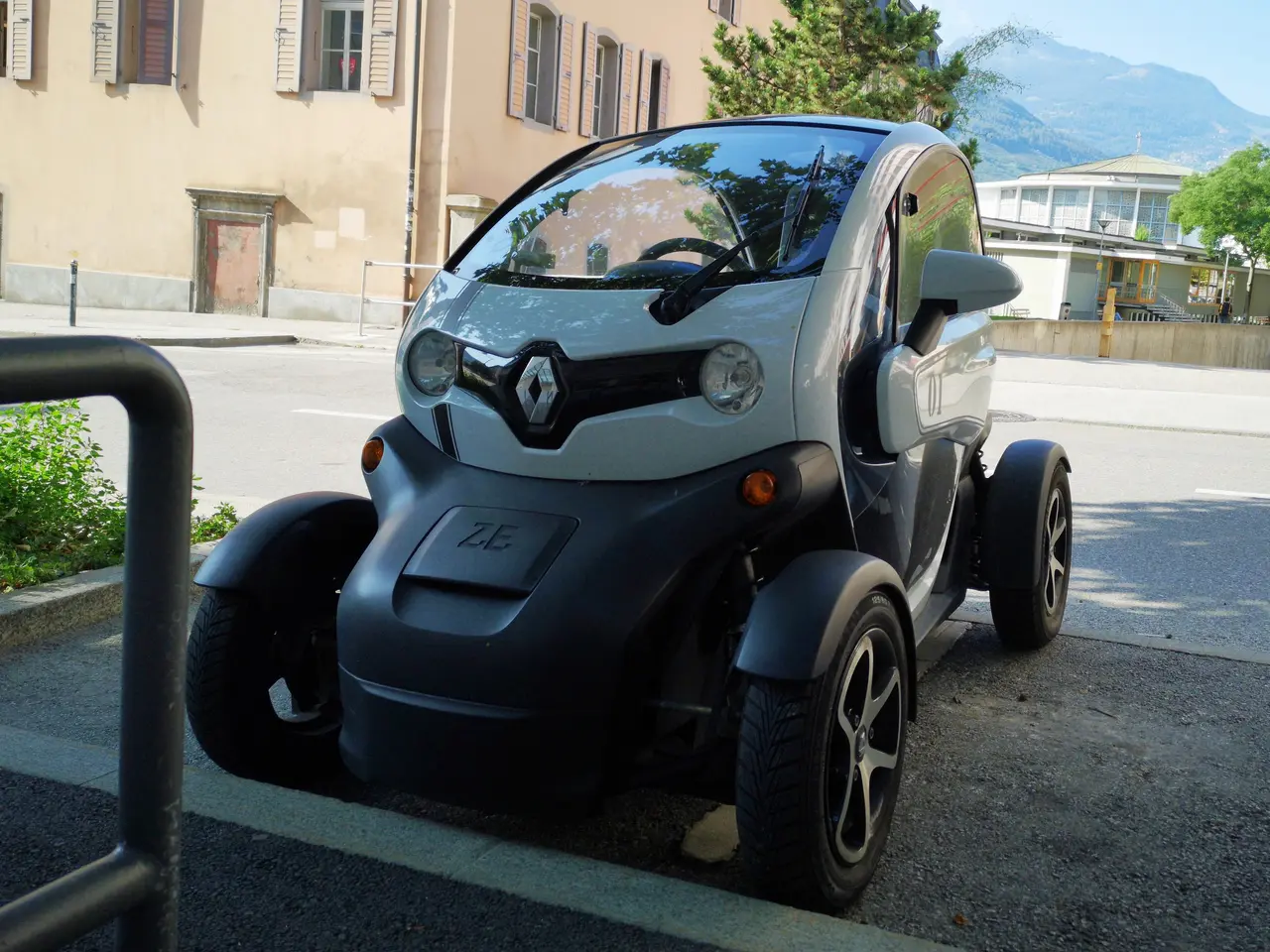 The image shows a Renault Twizy electric car parked on the side of the road in front of a building...