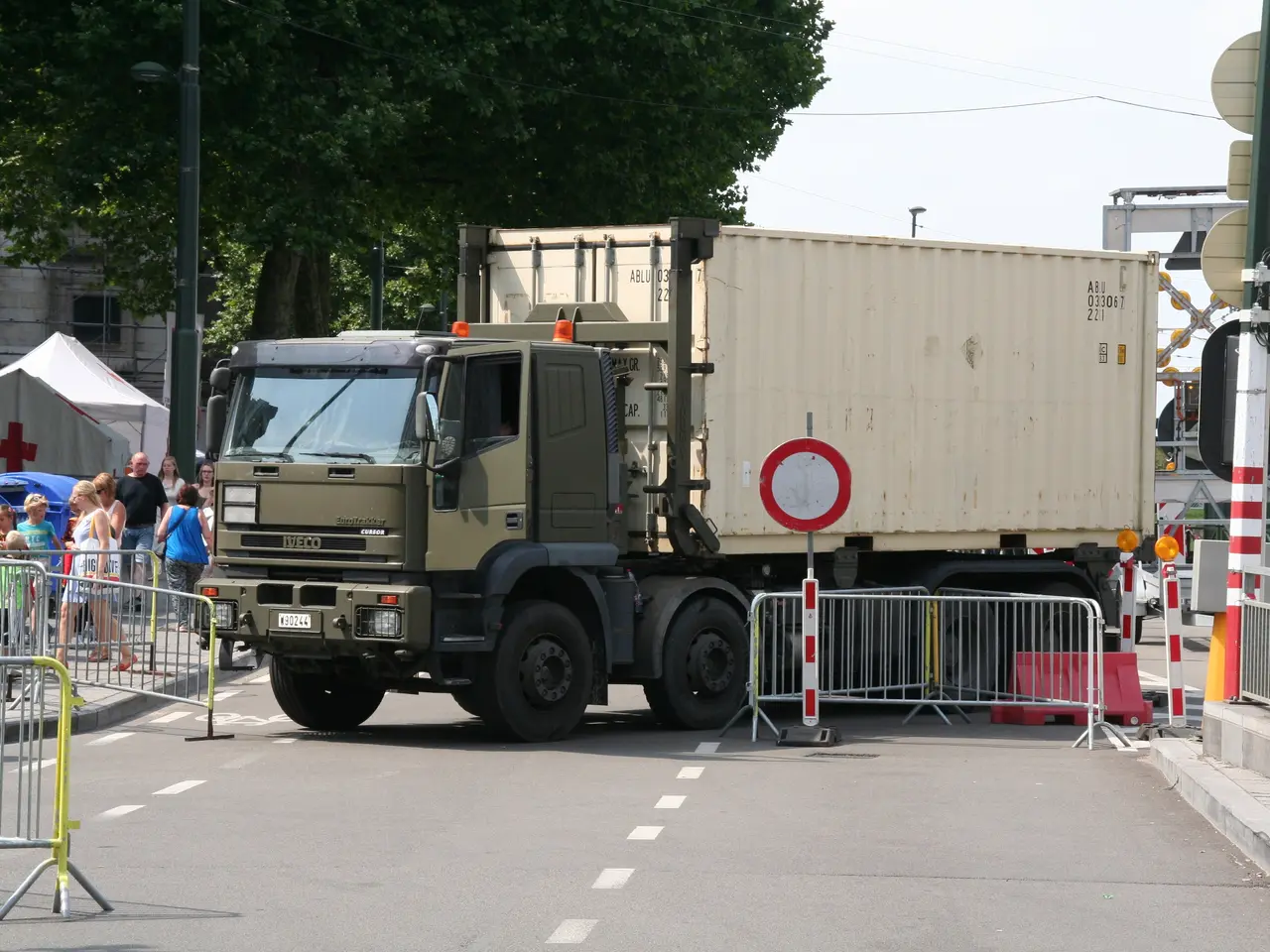 The image shows a truck parked on the side of the road, surrounded by a group of people standing on...