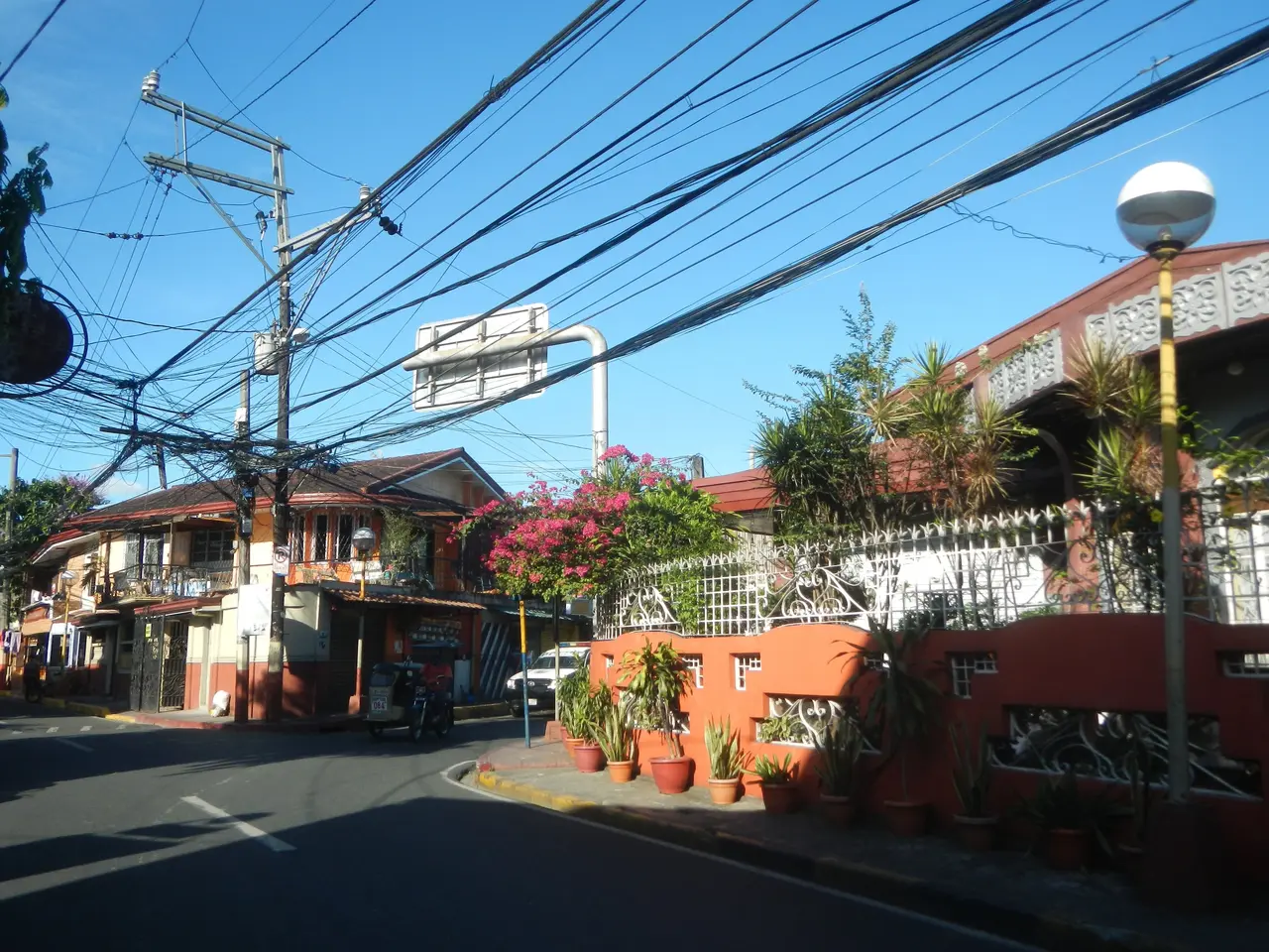 The image shows a street with power lines running down the middle of it, surrounded by buildings,...