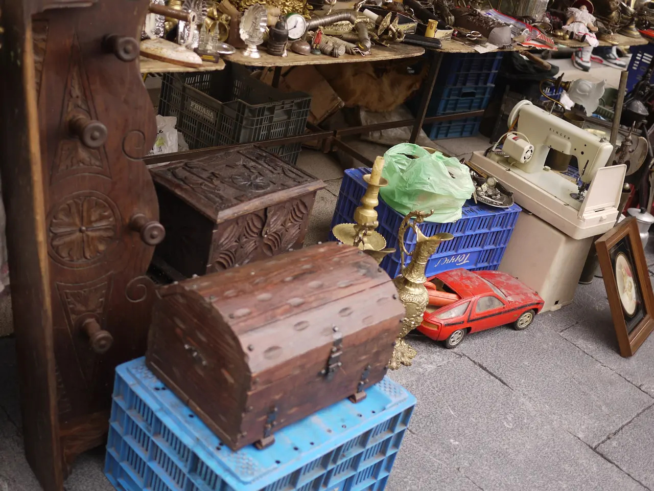 The image shows a flea market with a variety of items on display, including wooden boxes, a toy...