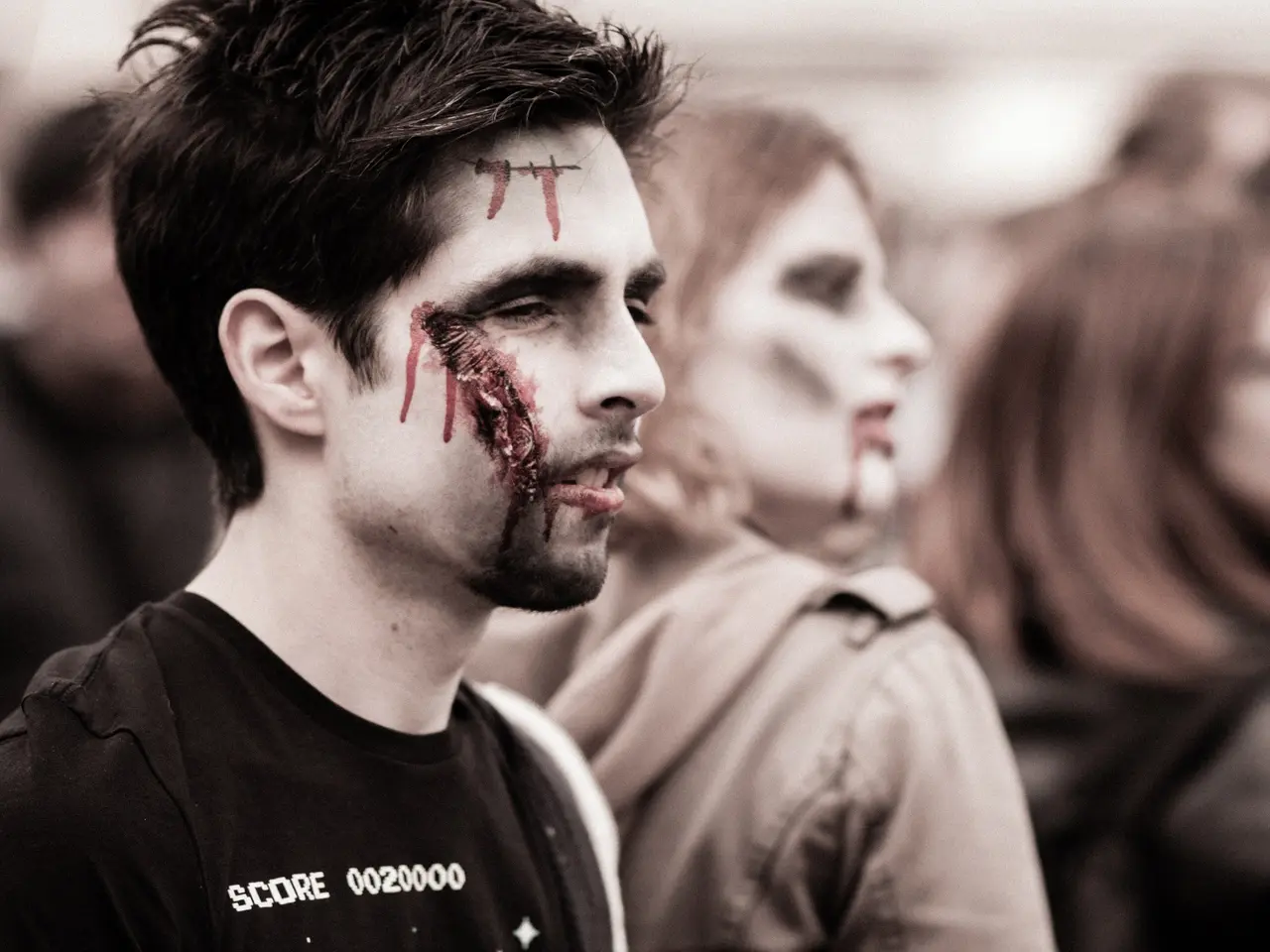 The image shows a group of people dressed up as zombies, with a man in the foreground wearing a...