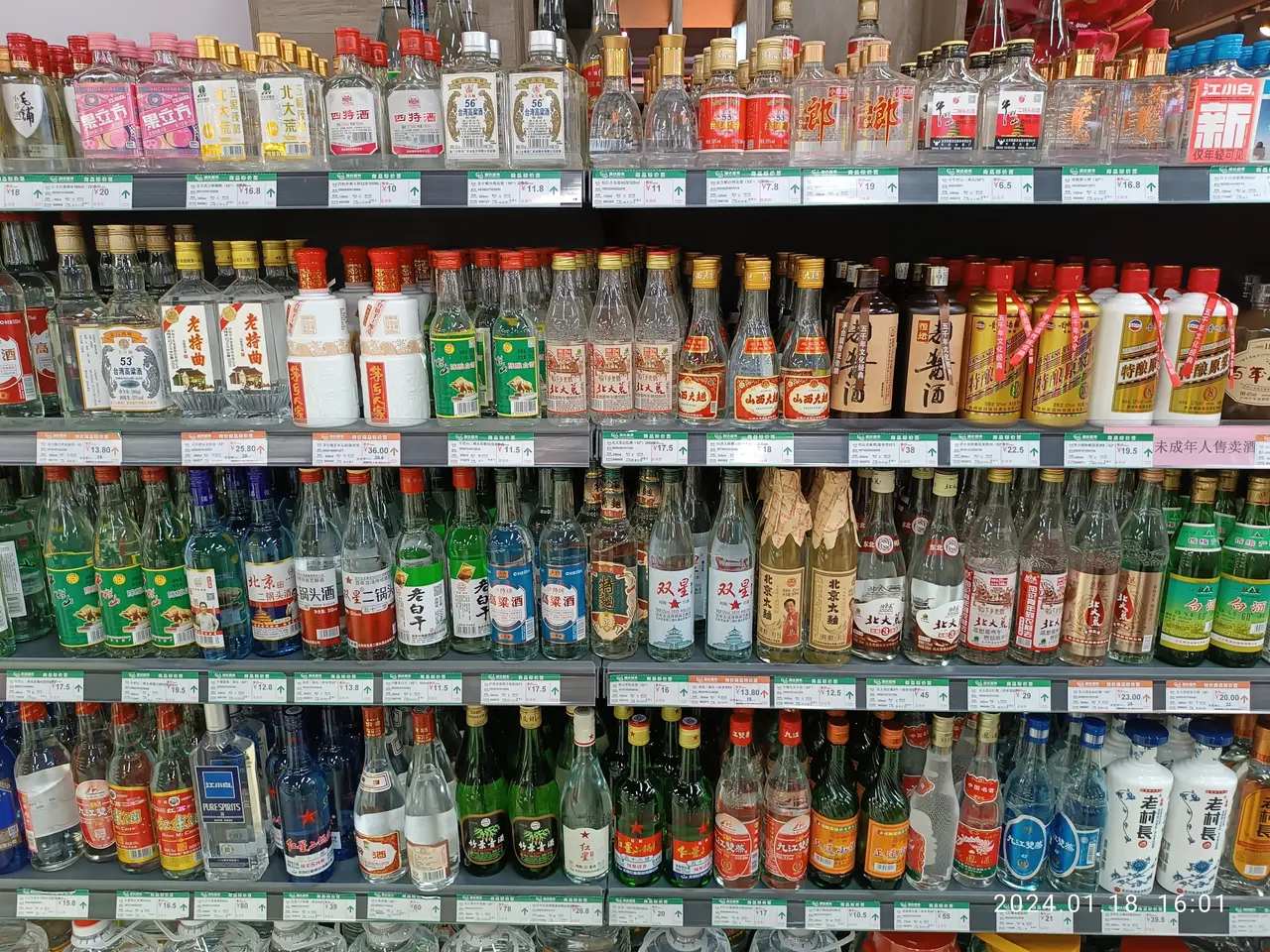 The image shows a display case filled with lots of different types of alcohol, including bottles...