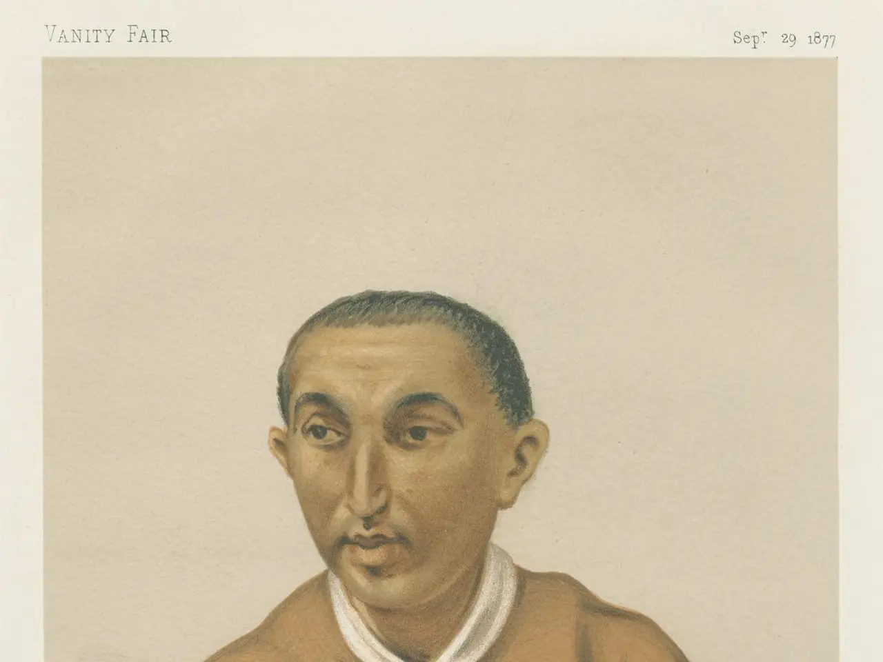 The image shows a man sitting at a table with his hands clasped in front of him. He is wearing a...