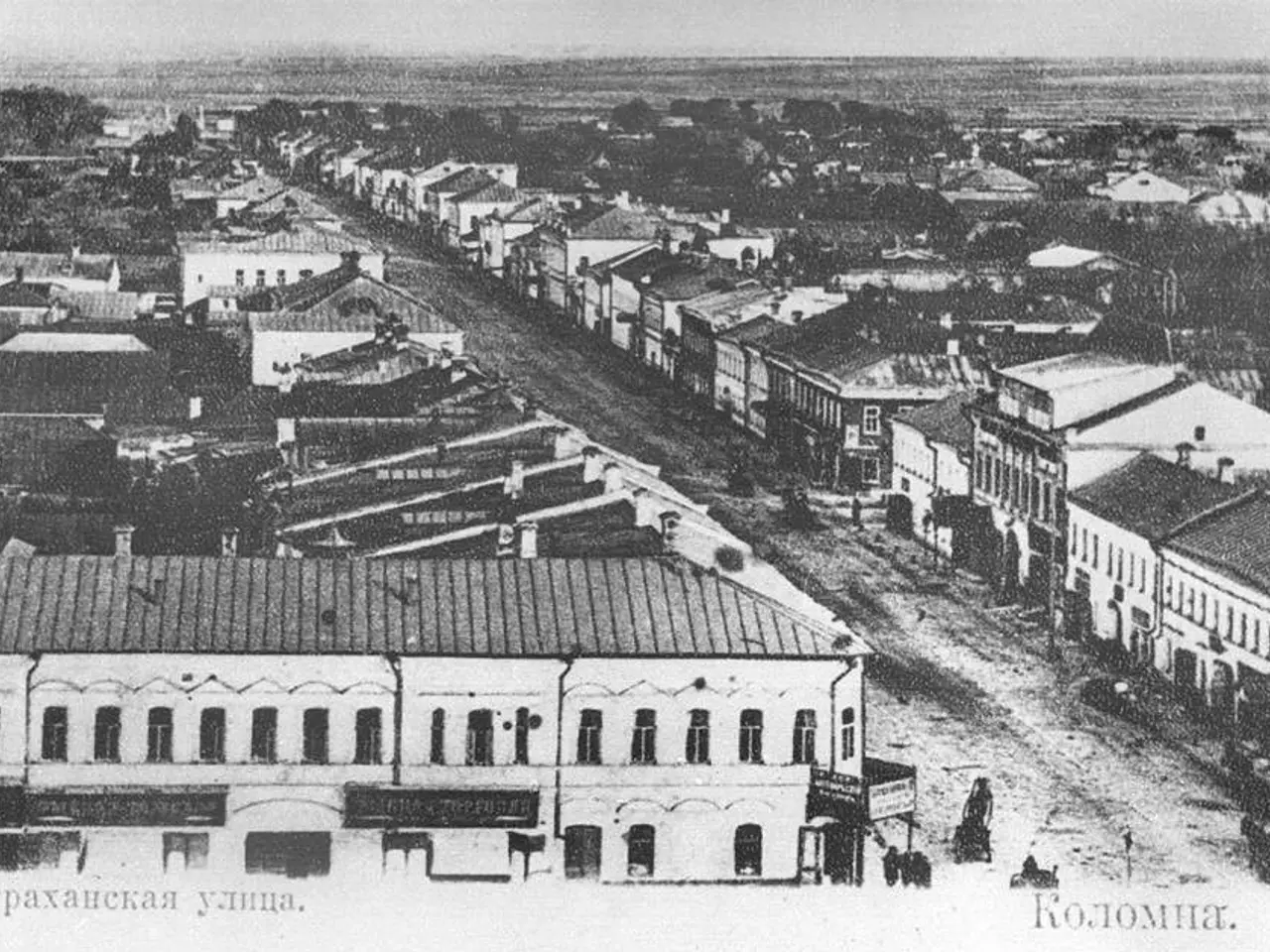The image shows an old black and white photo of a city street with buildings, trees, and people. At...