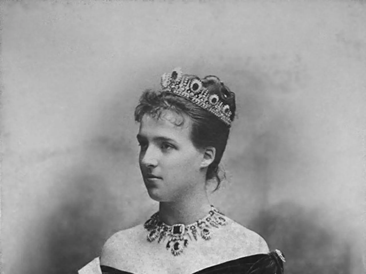 The image shows an old black and white photo of a woman wearing a dress and a crown. She has a...