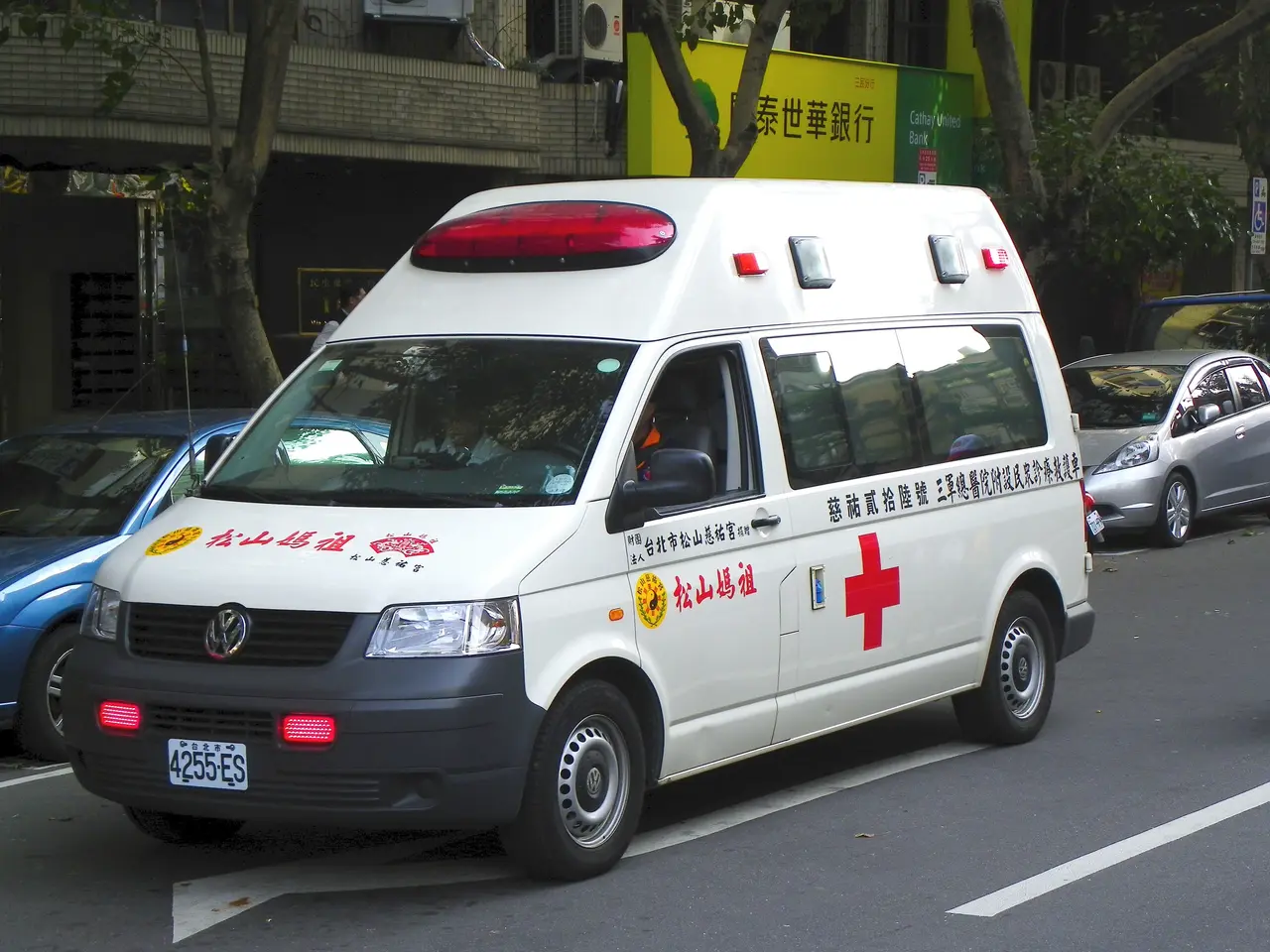 The image shows an ambulance parked on the side of the road, surrounded by other vehicles. In the...