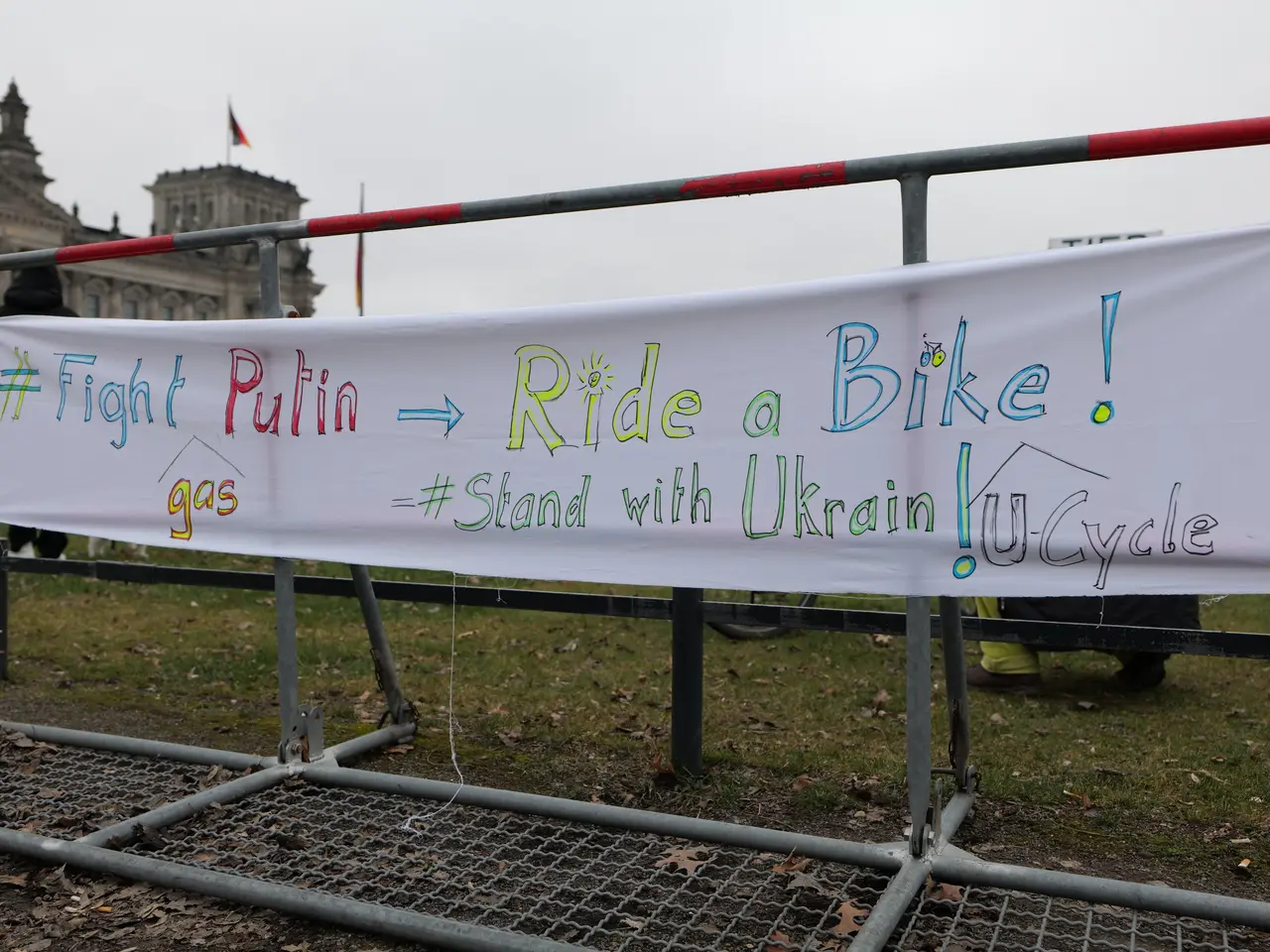 The image shows a group of people standing on the ground, holding a banner that reads "Fight Putin,...