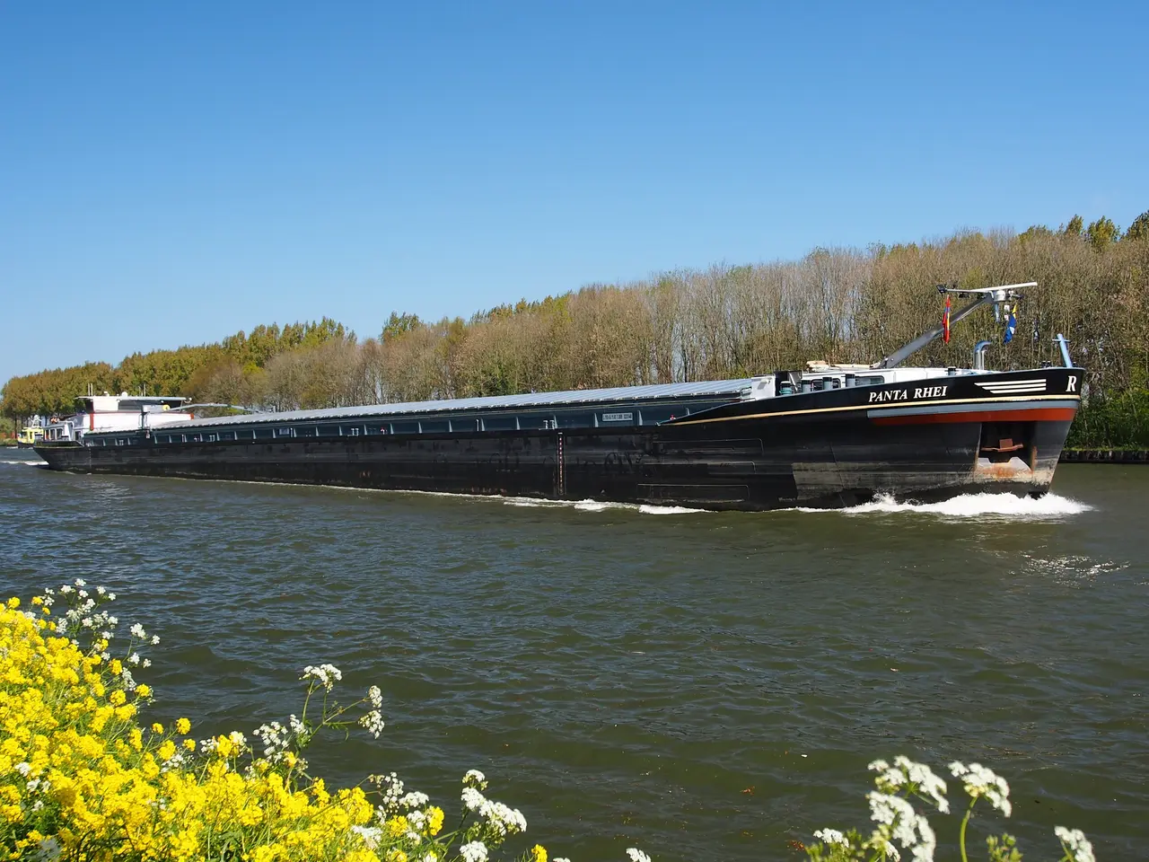 The image shows a large boat traveling down a river, surrounded by lush green trees and a bright...