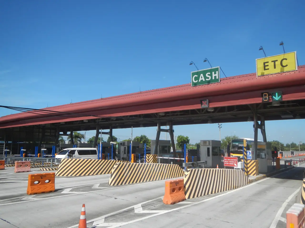 The image shows a toll booth with a sign that reads "Cash" on it, surrounded by vehicles on the...
