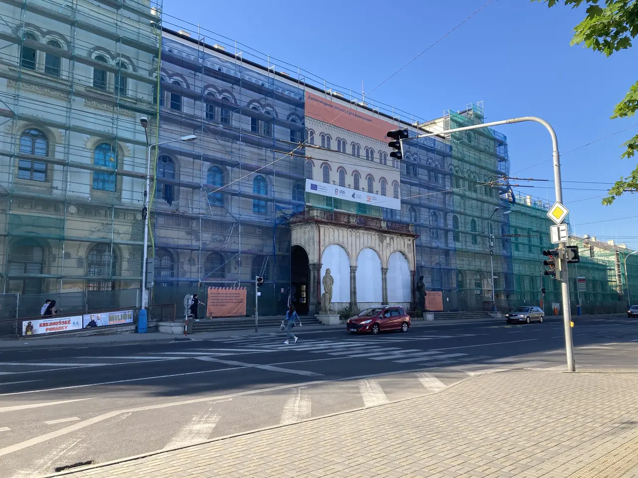 The image shows a large building with a lot of windows on the side of it, surrounded by vehicles on...