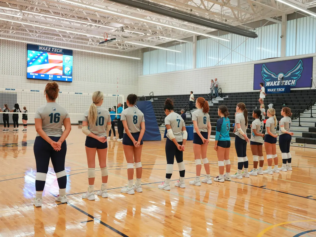 The image shows a group of women's volleyball players standing on top of a court, with a net in the...