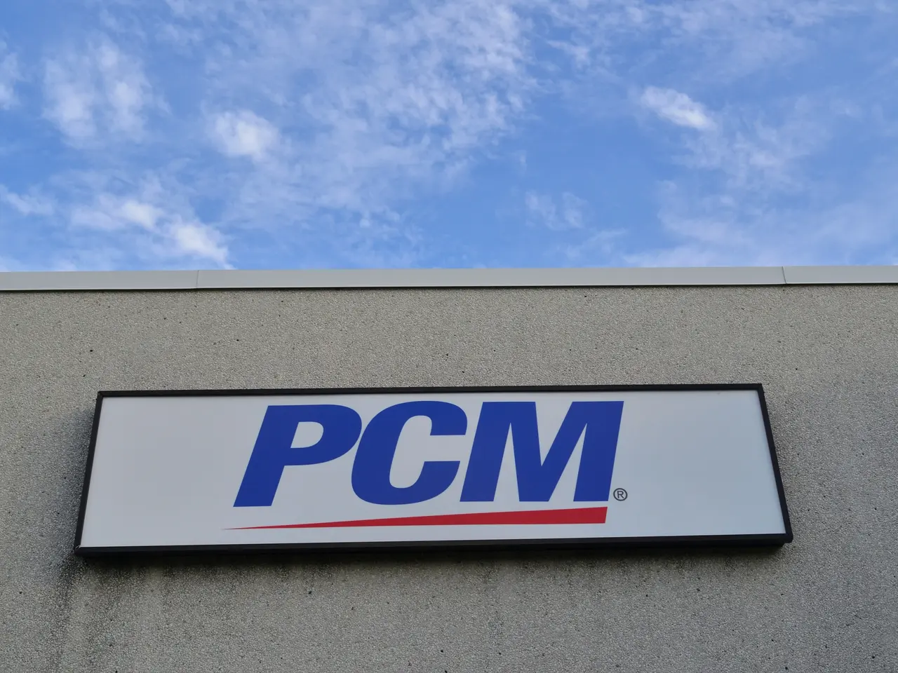 The image shows a PCM sign on the side of a building, with a board attached to the wall displaying...