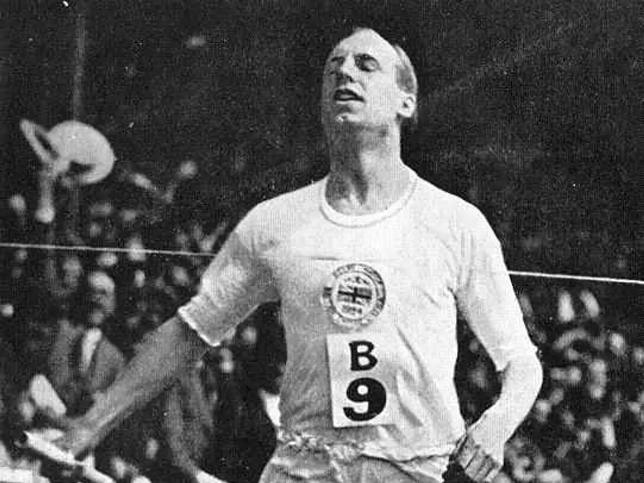 The image shows a black and white photo of a man running on a track, with a number on his t-shirt...