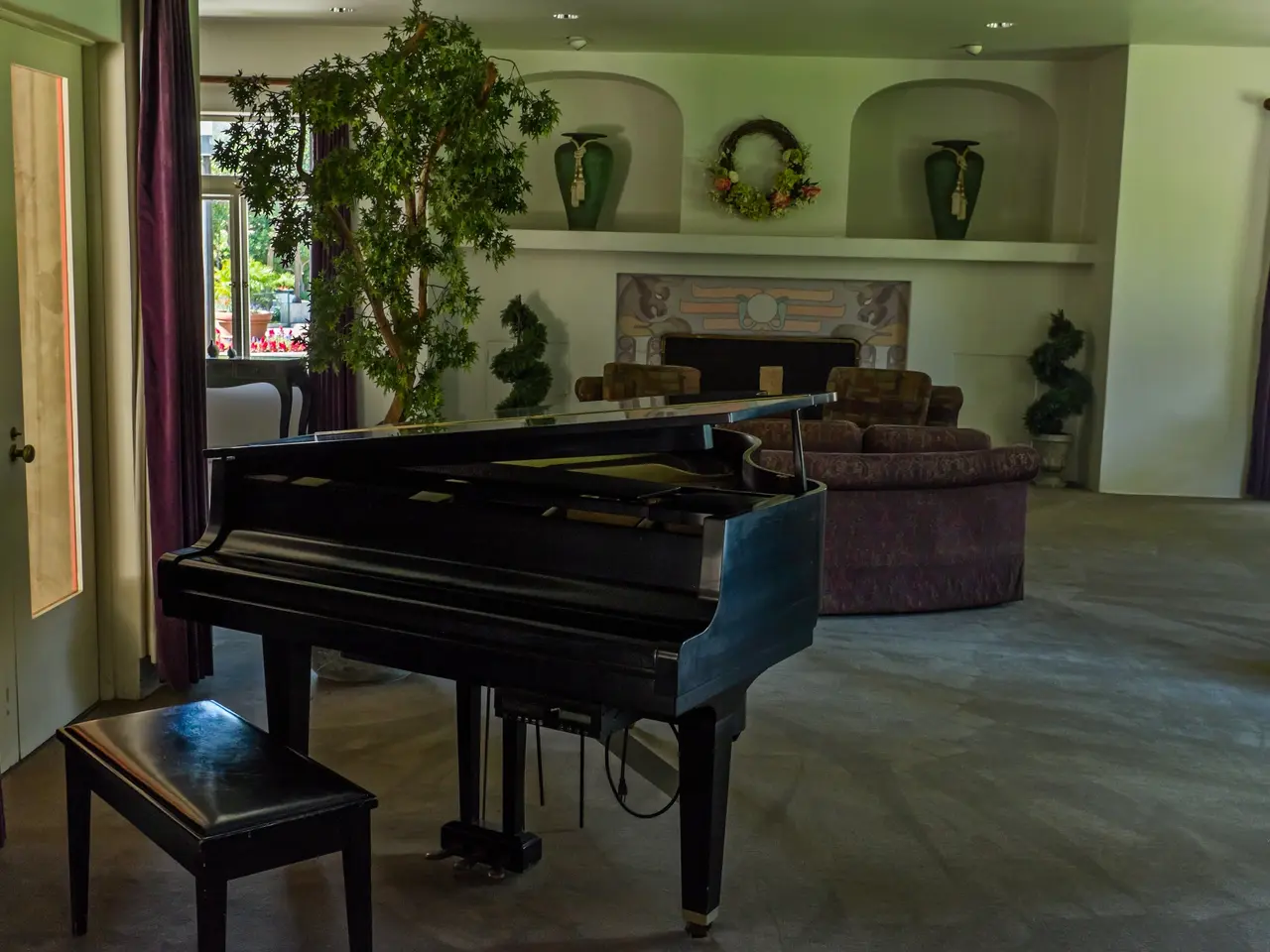 The image shows a living room with a grand piano in the center, surrounded by a bench, houseplants,...