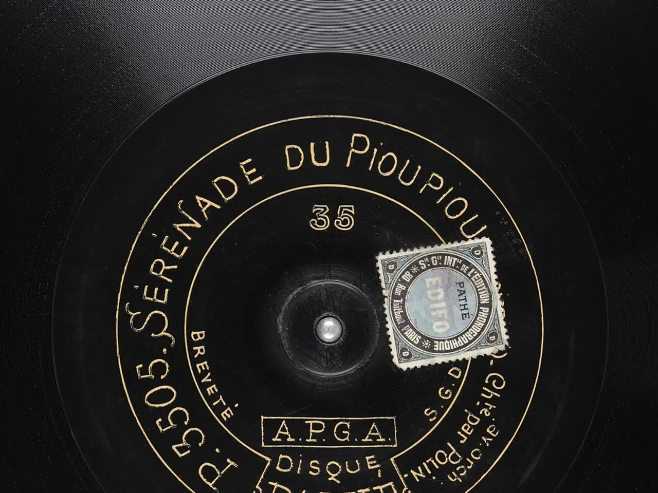 The image shows a black vinyl record with a gold label on it. The label has text and a stamp on it,...