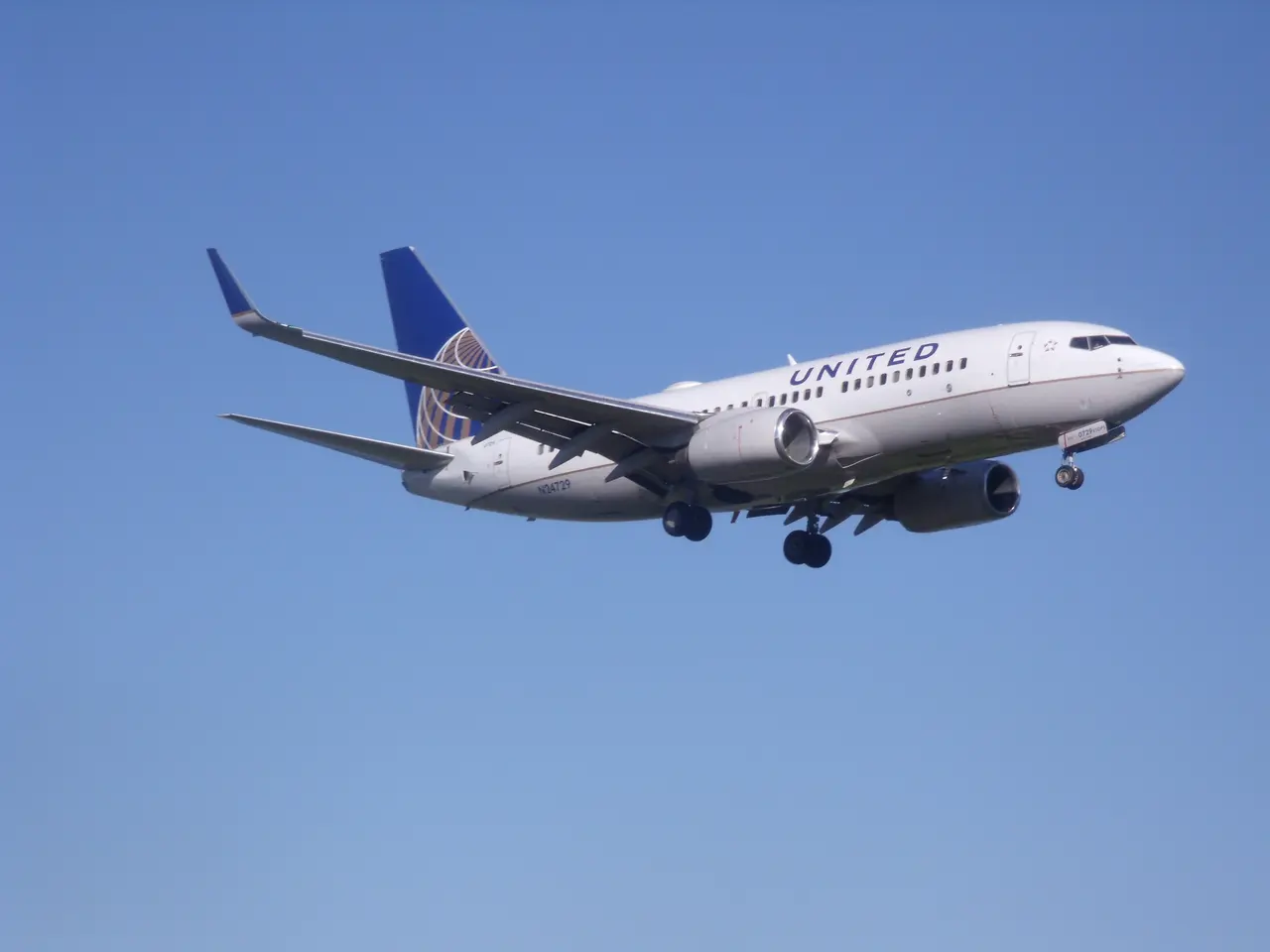The image shows a United Airlines Boeing 737-800 in flight, with its white and blue livery standing...