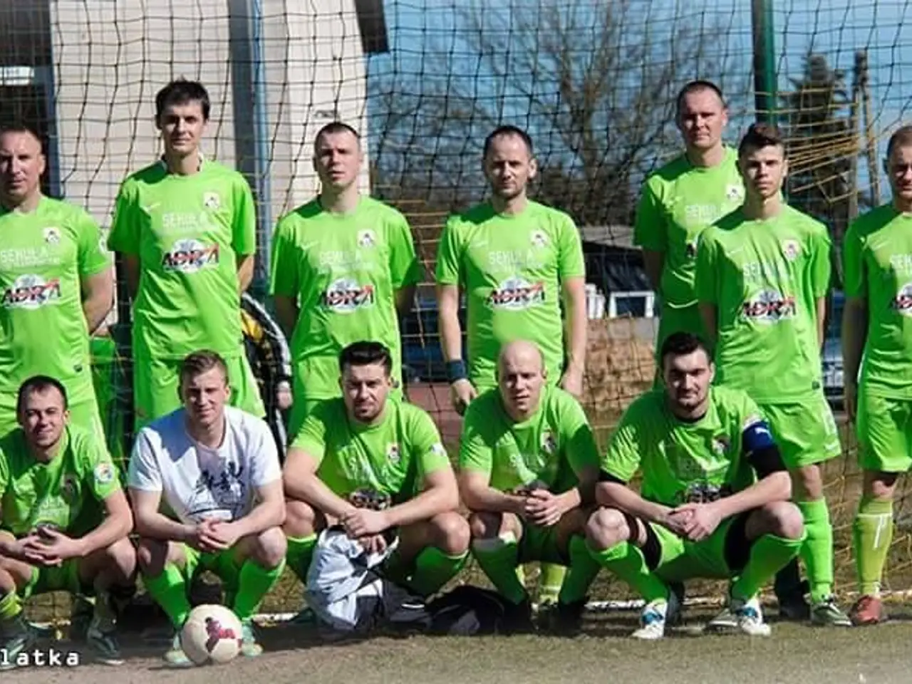The image shows a group of men standing next to each other on a soccer field. They are wearing...