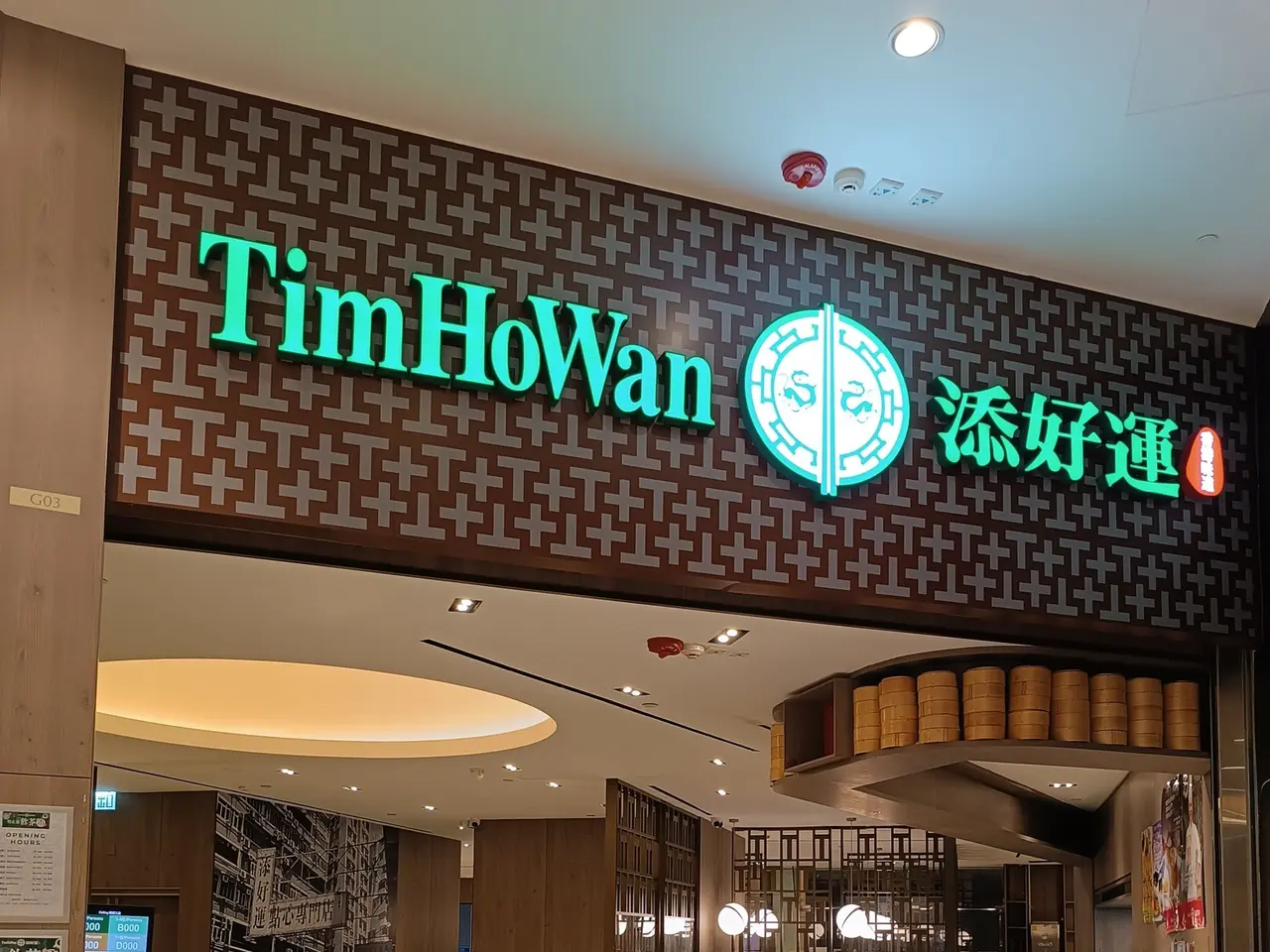 The image shows a Tim Howan restaurant in Hong Kong, with people sitting on chairs and some...