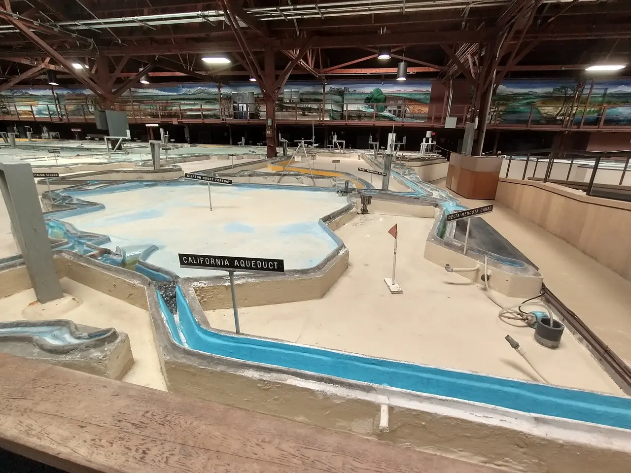 The image shows a large indoor water park with a lot of water slides, poles, boards with text,...