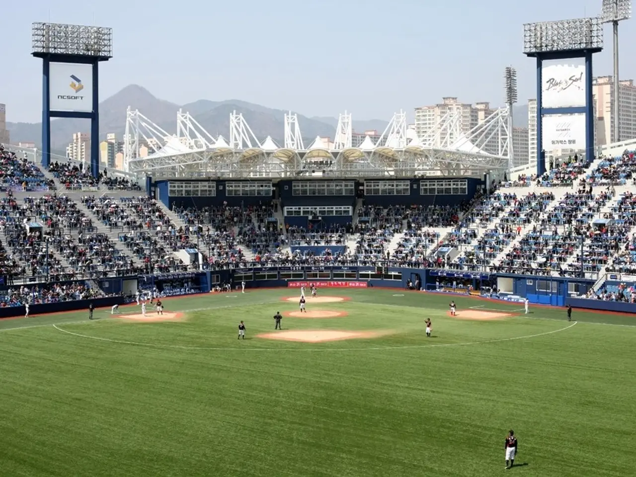 The image shows a baseball game being played in a stadium, with a group of people on the ground and...