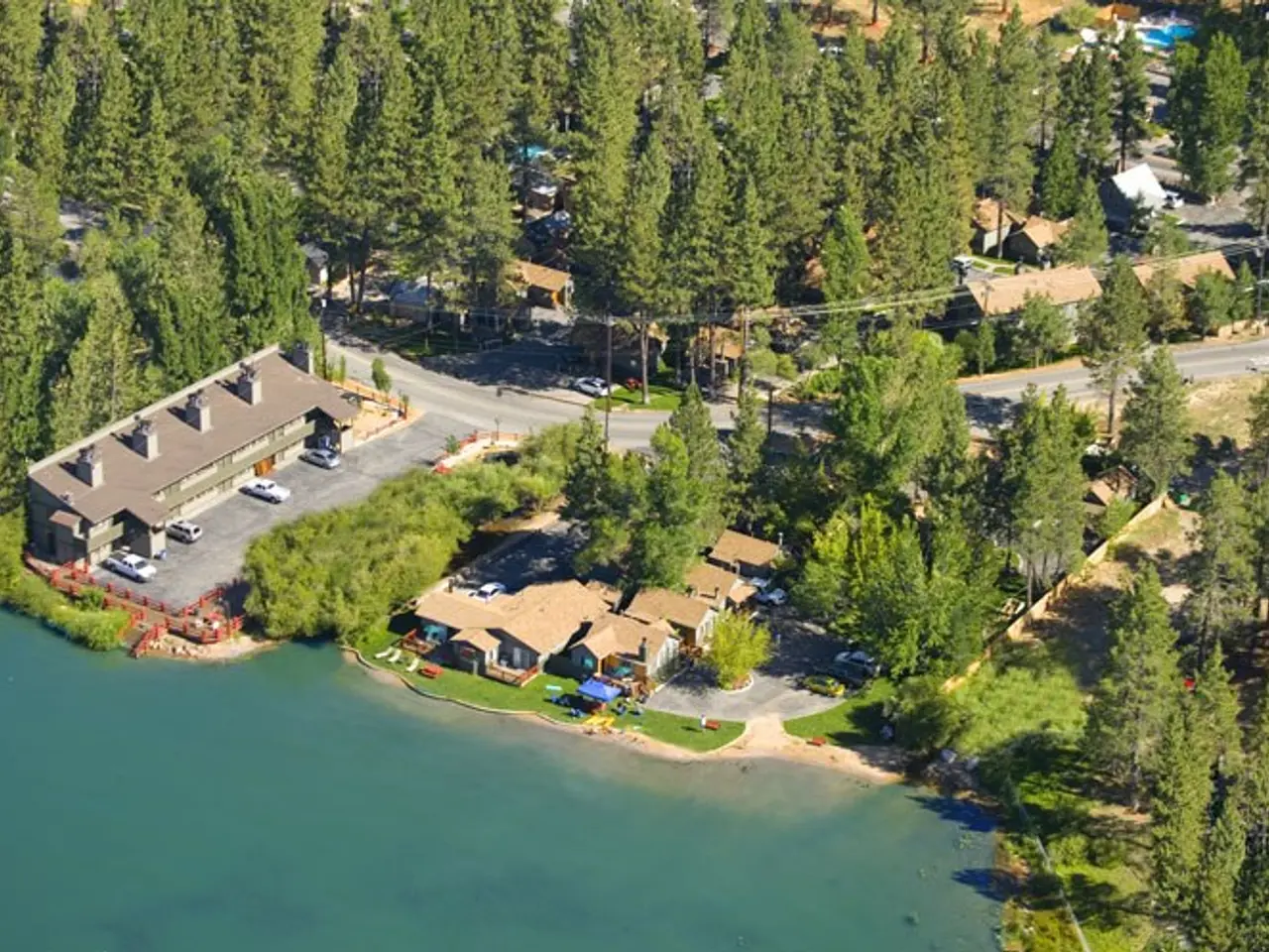 The image shows an aerial view of a resort situated on the shore of a lake, surrounded by trees,...
