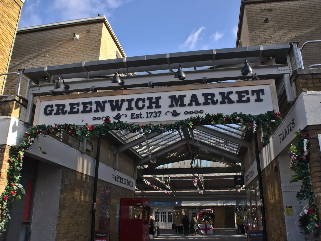The image shows the entrance to Greenwich Market in London, England. It is an arch with text on it,...