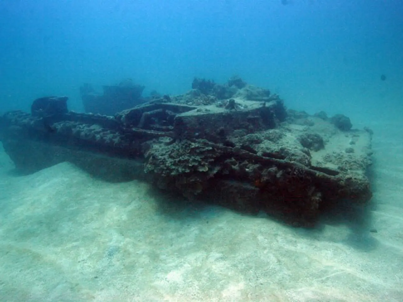 The image shows an old rusty tank submerged in the ocean, surrounded by a variety of fish. The tank...