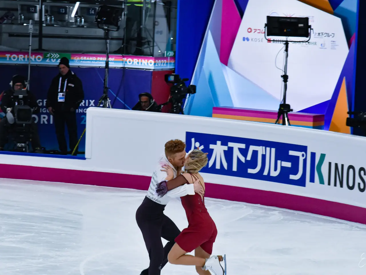 The image shows a couple of people skating on an ice rink, embracing each other in a loving...