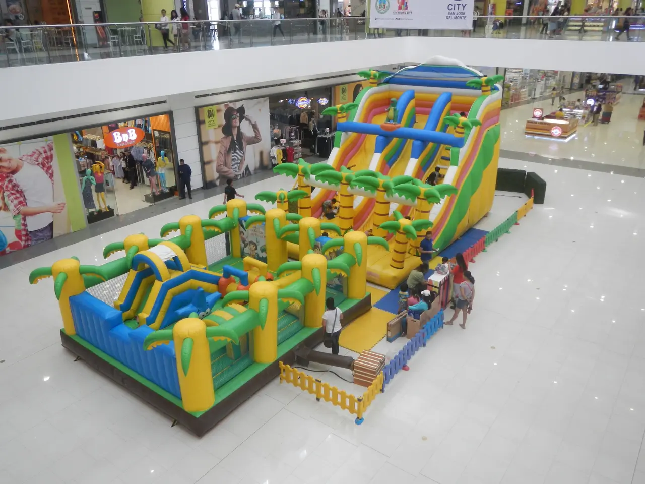 The image shows a large inflatable water park in the middle of a shopping mall. There are several...