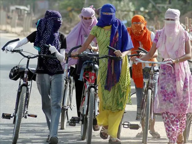 In the center of the image some ladies are walking by holding bicycle and wearing scarf. In the...
