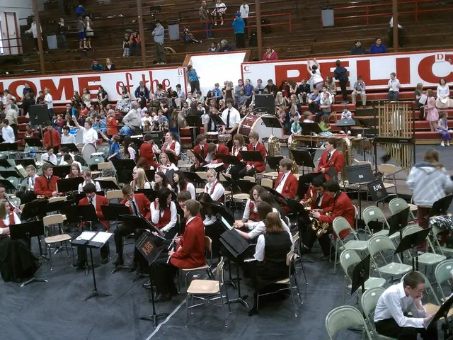 In this picture there is a group of boys and girls sitting on the chairs in the stadium ground for...