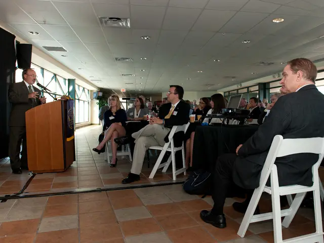This picture shows some people sitting in the chairs in front of a man who is standing near the...